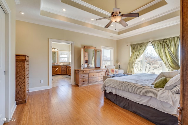 bedroom featuring connected bathroom, light wood-style flooring, baseboards, a tray ceiling, and crown molding