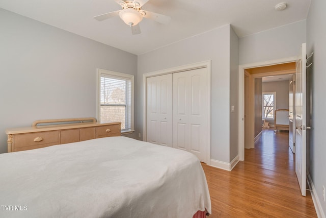 bedroom featuring a ceiling fan, light wood-type flooring, a closet, and baseboards