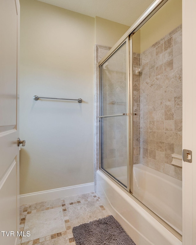 bathroom featuring combined bath / shower with glass door and baseboards