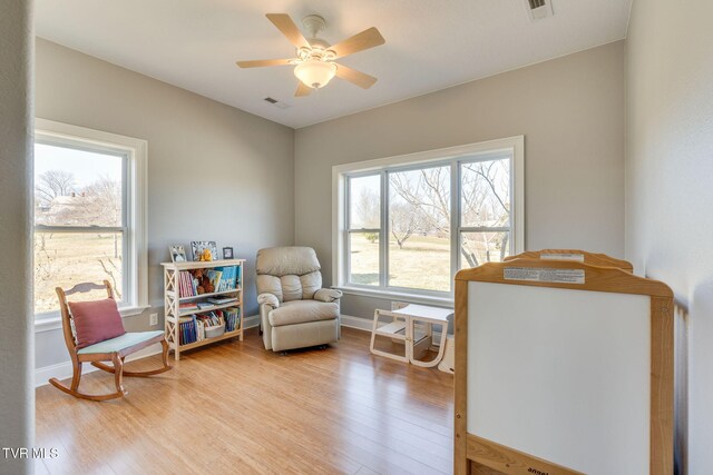 living area with light wood finished floors, ceiling fan, visible vents, and baseboards