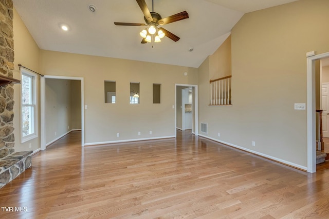 unfurnished living room with light wood-type flooring, vaulted ceiling, ceiling fan, and a stone fireplace