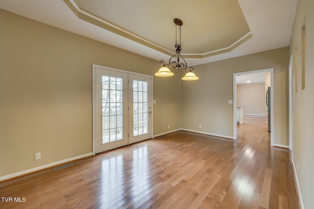 spare room featuring a chandelier, french doors, light hardwood / wood-style floors, and a raised ceiling