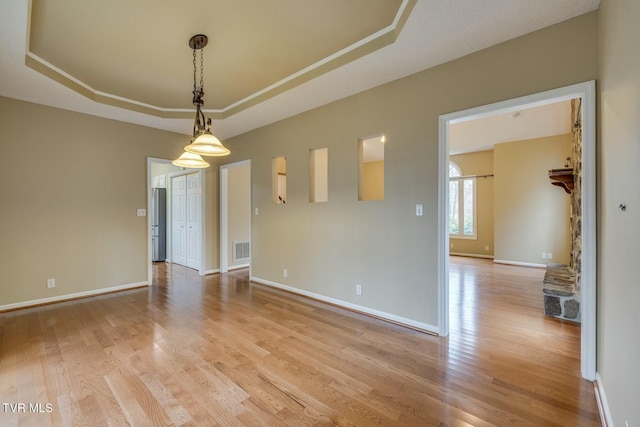 spare room featuring a stone fireplace, a raised ceiling, and light hardwood / wood-style flooring