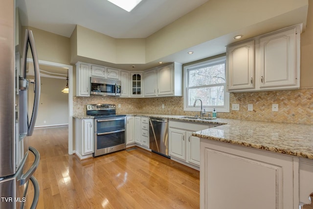 kitchen with white cabinets, appliances with stainless steel finishes, light stone counters, and sink