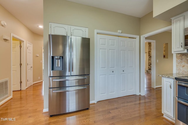 kitchen featuring white cabinets, appliances with stainless steel finishes, decorative backsplash, and light stone countertops