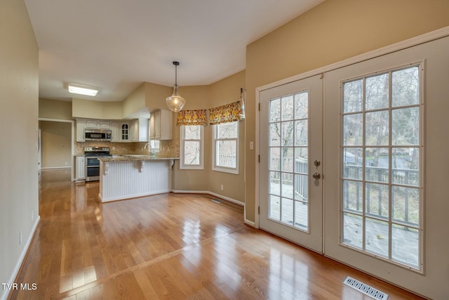 kitchen featuring backsplash, hanging light fixtures, stainless steel appliances, and light hardwood / wood-style floors