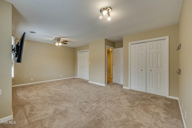 unfurnished bedroom with multiple closets, light carpet, and ceiling fan