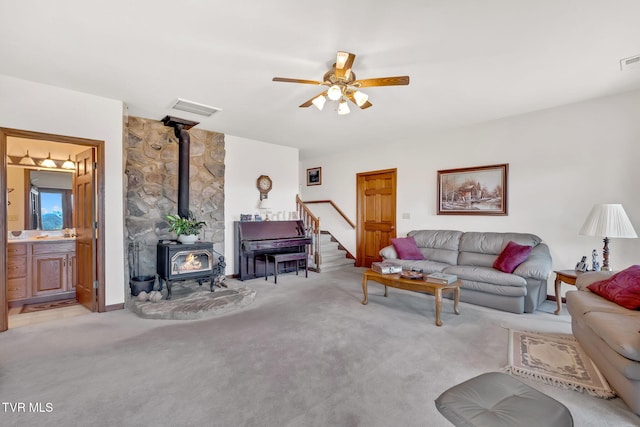 carpeted living room with ceiling fan and a wood stove