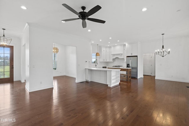 unfurnished living room with ceiling fan with notable chandelier, crown molding, dark wood-type flooring, and sink