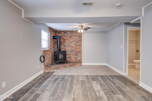 unfurnished living room featuring a textured ceiling, a wood stove, and ceiling fan