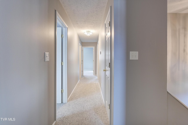 corridor with a textured ceiling and light carpet