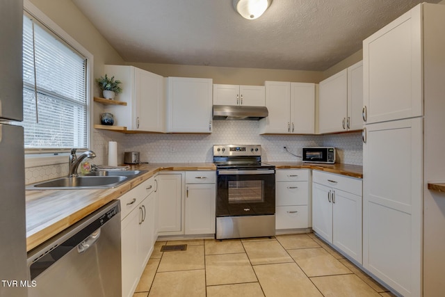 kitchen with a textured ceiling, stainless steel appliances, sink, butcher block countertops, and white cabinetry