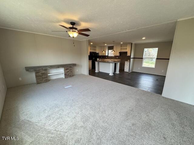 unfurnished living room with ceiling fan, a fireplace, dark carpet, and a textured ceiling