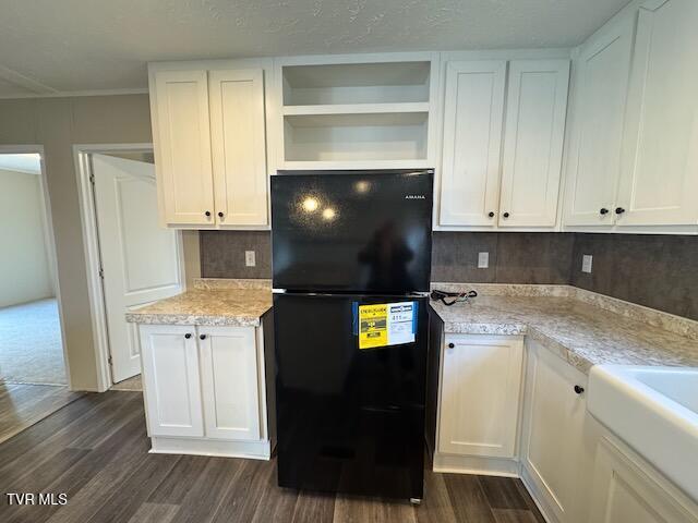 kitchen with white cabinets, dark hardwood / wood-style floors, black fridge, and light stone counters