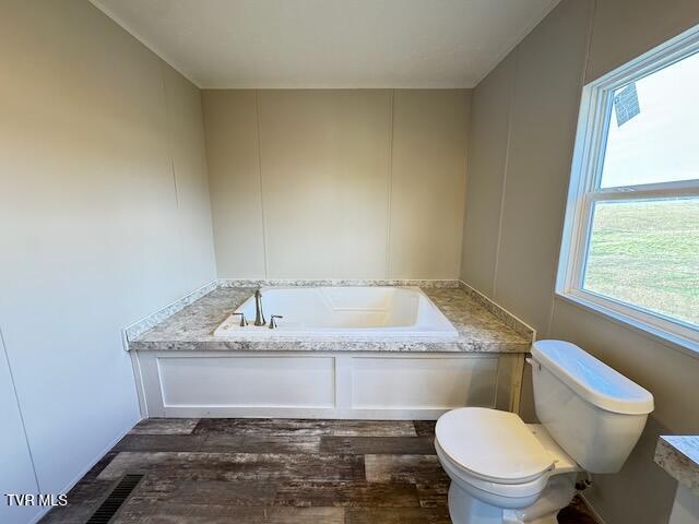 bathroom with toilet, wood-type flooring, and a bath