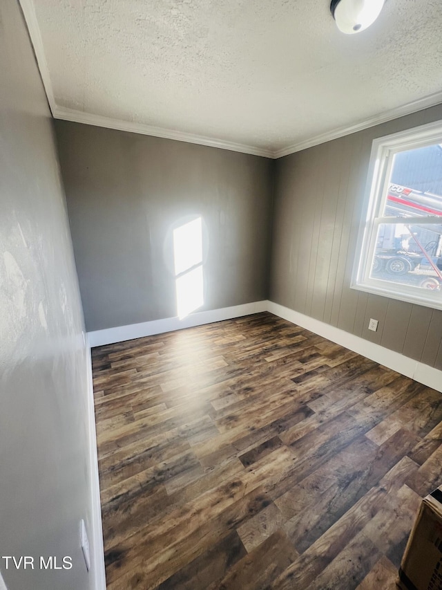 empty room with a textured ceiling, crown molding, and dark wood-type flooring