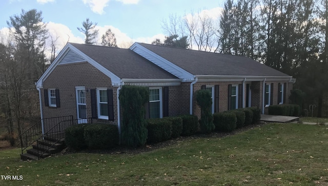 view of front of home with brick siding, a shingled roof, and a front lawn