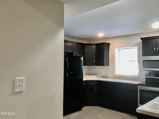 kitchen featuring light tile patterned floors, stainless steel appliances, dark cabinetry, and light countertops