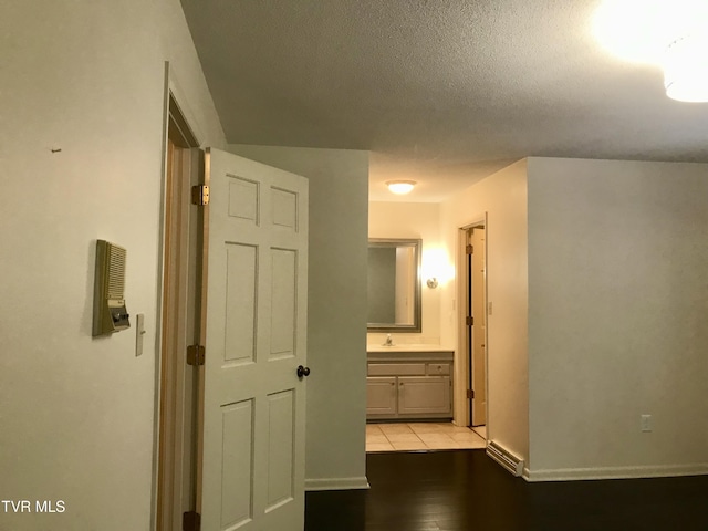 hall featuring a sink, baseboards, light wood finished floors, and a textured ceiling