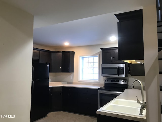 kitchen with light countertops, light tile patterned floors, appliances with stainless steel finishes, dark cabinetry, and a sink