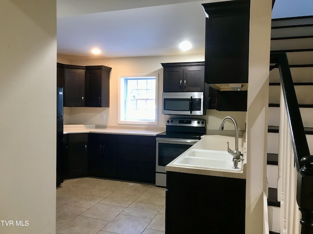 kitchen with light tile patterned floors, a sink, light countertops, appliances with stainless steel finishes, and dark cabinets