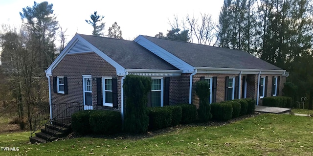 view of front facade with a front yard, brick siding, and roof with shingles