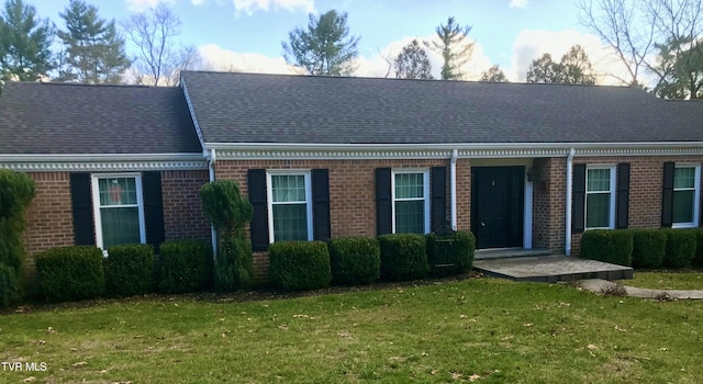 view of front of house with brick siding, a front lawn, and roof with shingles