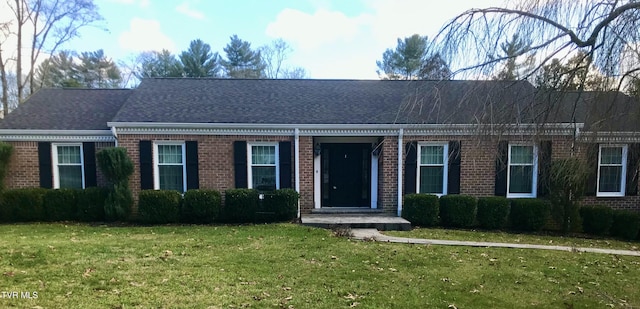 view of front facade with brick siding, a front yard, and roof with shingles