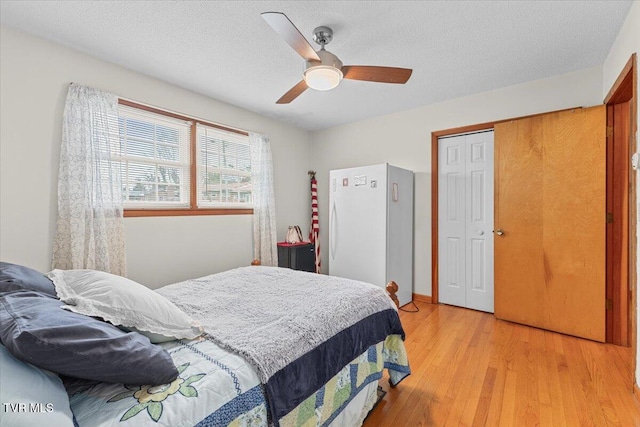 bedroom with ceiling fan, white refrigerator, light hardwood / wood-style floors, a textured ceiling, and a closet