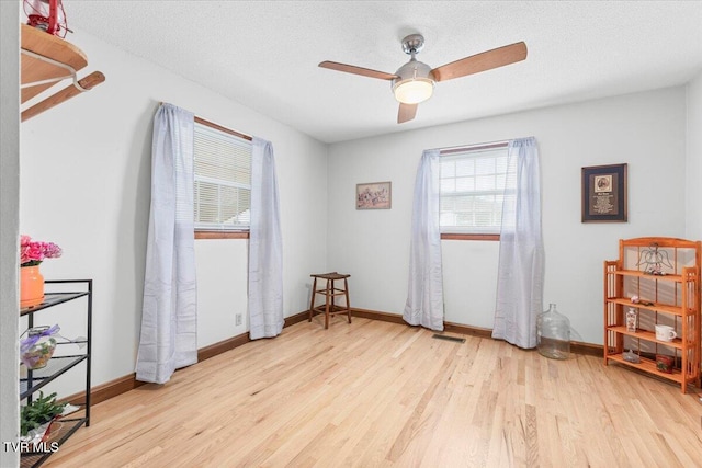 empty room with ceiling fan, light wood-type flooring, and a textured ceiling