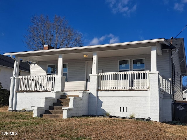 bungalow-style home with brick siding, covered porch, a chimney, and a front yard