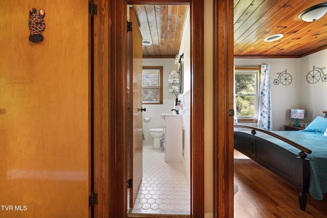 bedroom featuring hardwood / wood-style flooring, ensuite bathroom, wood ceiling, and tile walls