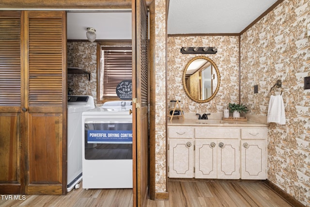 washroom featuring a textured ceiling, crown molding, sink, washer and dryer, and light hardwood / wood-style flooring