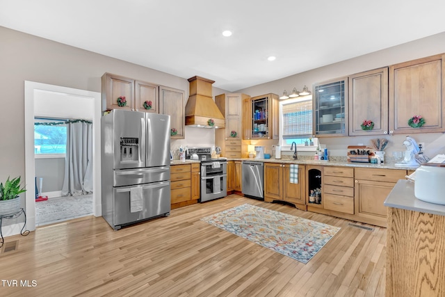 kitchen with sink, premium range hood, light brown cabinetry, appliances with stainless steel finishes, and light wood-type flooring