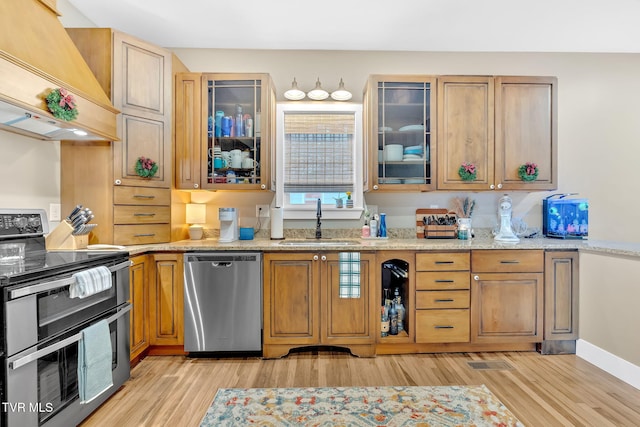 kitchen featuring light stone countertops, appliances with stainless steel finishes, light wood-type flooring, custom range hood, and sink