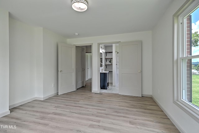 unfurnished bedroom featuring a closet, a walk in closet, light hardwood / wood-style floors, and multiple windows