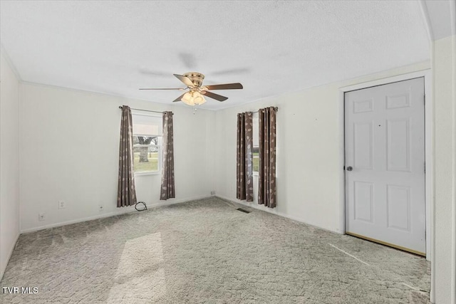 empty room with ceiling fan, light colored carpet, and a textured ceiling