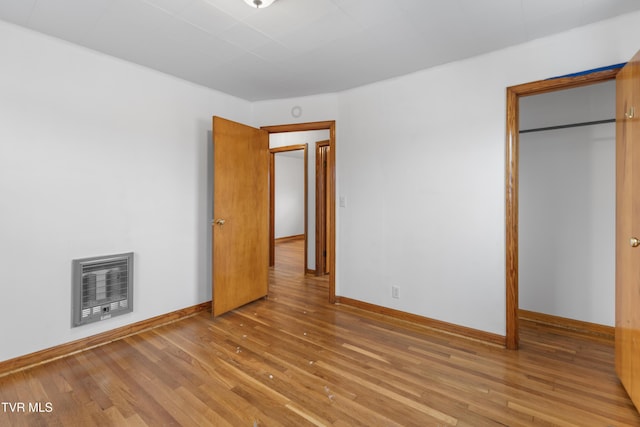 unfurnished bedroom featuring a closet, hardwood / wood-style floors, and heating unit