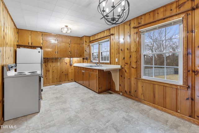 kitchen featuring sink, wood walls, decorative light fixtures, a wealth of natural light, and white appliances