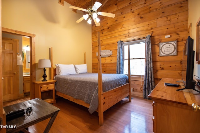 bedroom with ensuite bath, ceiling fan, vaulted ceiling with beams, and hardwood / wood-style flooring