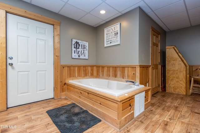 bathroom featuring a paneled ceiling, wood-type flooring, and a tub