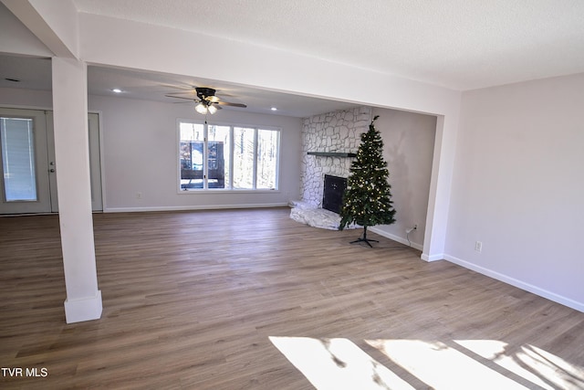 unfurnished living room with a textured ceiling, ceiling fan, a fireplace, and light hardwood / wood-style flooring