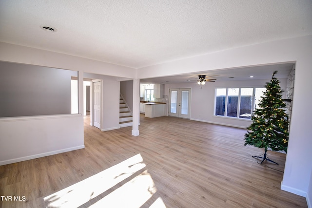 unfurnished living room with ceiling fan, french doors, a textured ceiling, and light wood-type flooring