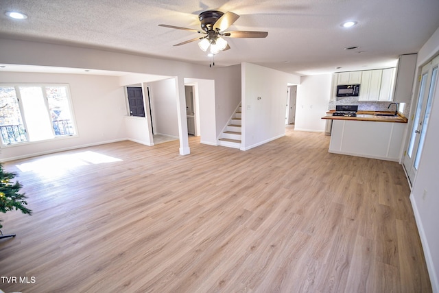 unfurnished living room featuring a textured ceiling, light hardwood / wood-style flooring, ceiling fan, and sink