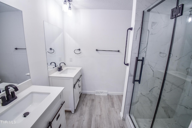 bathroom with vanity, a shower with shower door, a textured ceiling, and wood-type flooring