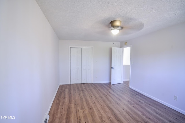 unfurnished bedroom featuring ceiling fan, wood-type flooring, a textured ceiling, and a closet