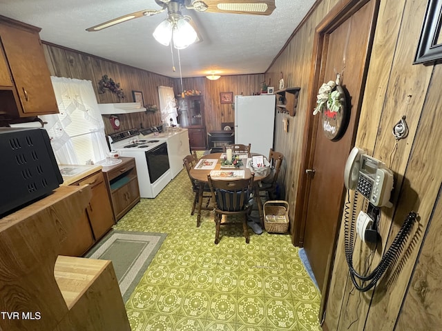 kitchen with ceiling fan, wood walls, white appliances, and a textured ceiling