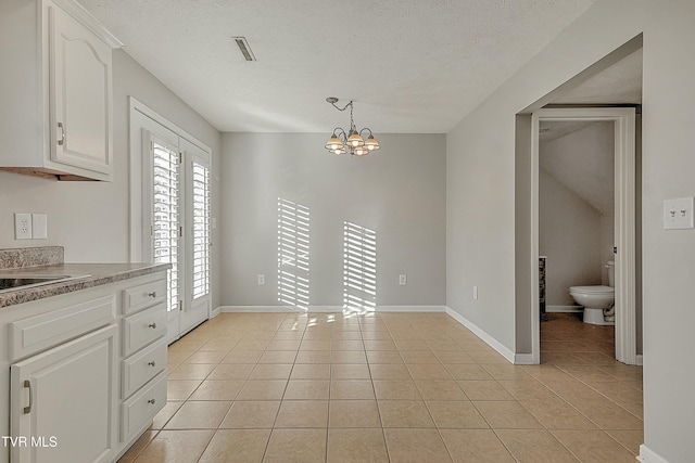 unfurnished dining area with light tile patterned floors, a textured ceiling, and a notable chandelier