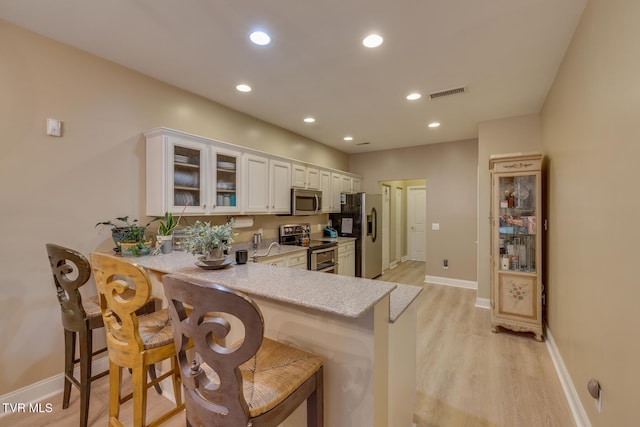 kitchen with kitchen peninsula, a kitchen bar, stainless steel appliances, and white cabinetry