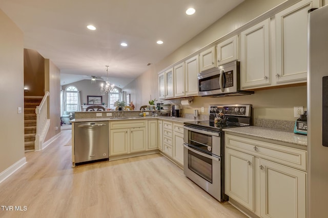 kitchen featuring kitchen peninsula, appliances with stainless steel finishes, pendant lighting, cream cabinets, and light hardwood / wood-style floors